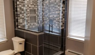 Modern bathroom with glass shower and dark tile flooring.